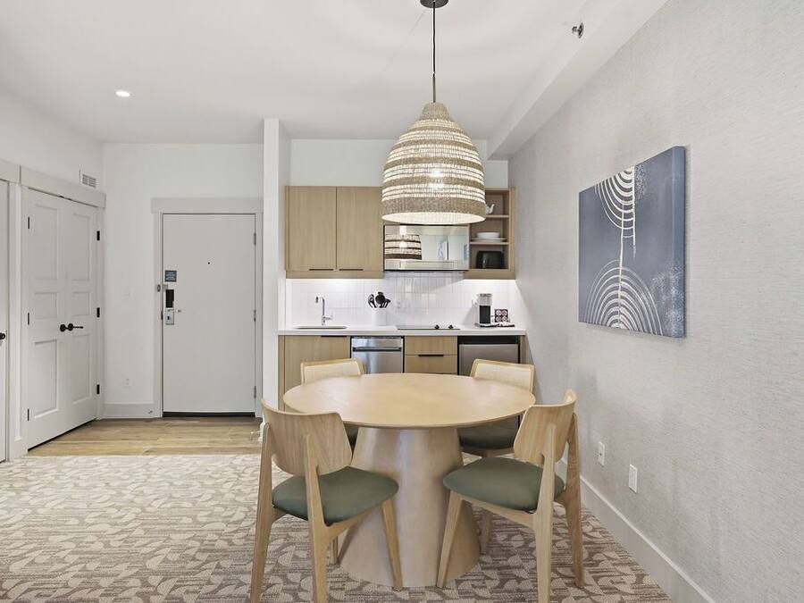 Una cocina moderna con gabinetes blancos, una mesa redonda de comedor y una lámpara colgante.