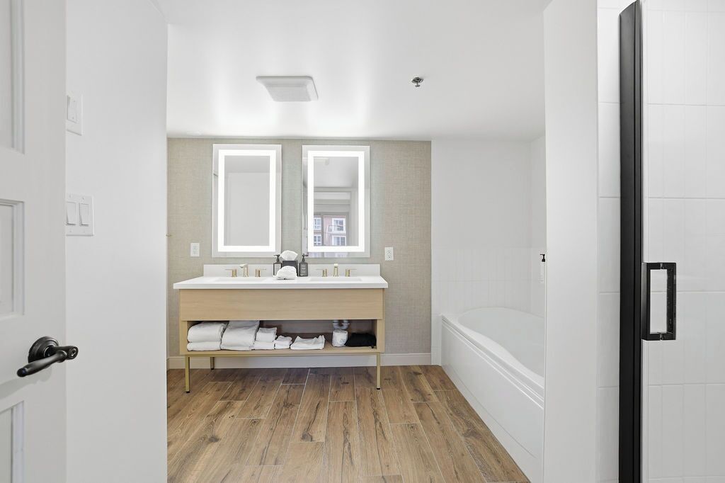 A modern bathroom with a double vanity, a bathtub, and a wooden floor.