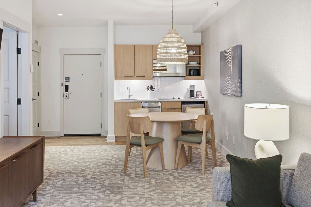 A modern kitchen with wooden cabinets, a central island with chairs, a hanging pendant light, and a dining table.
