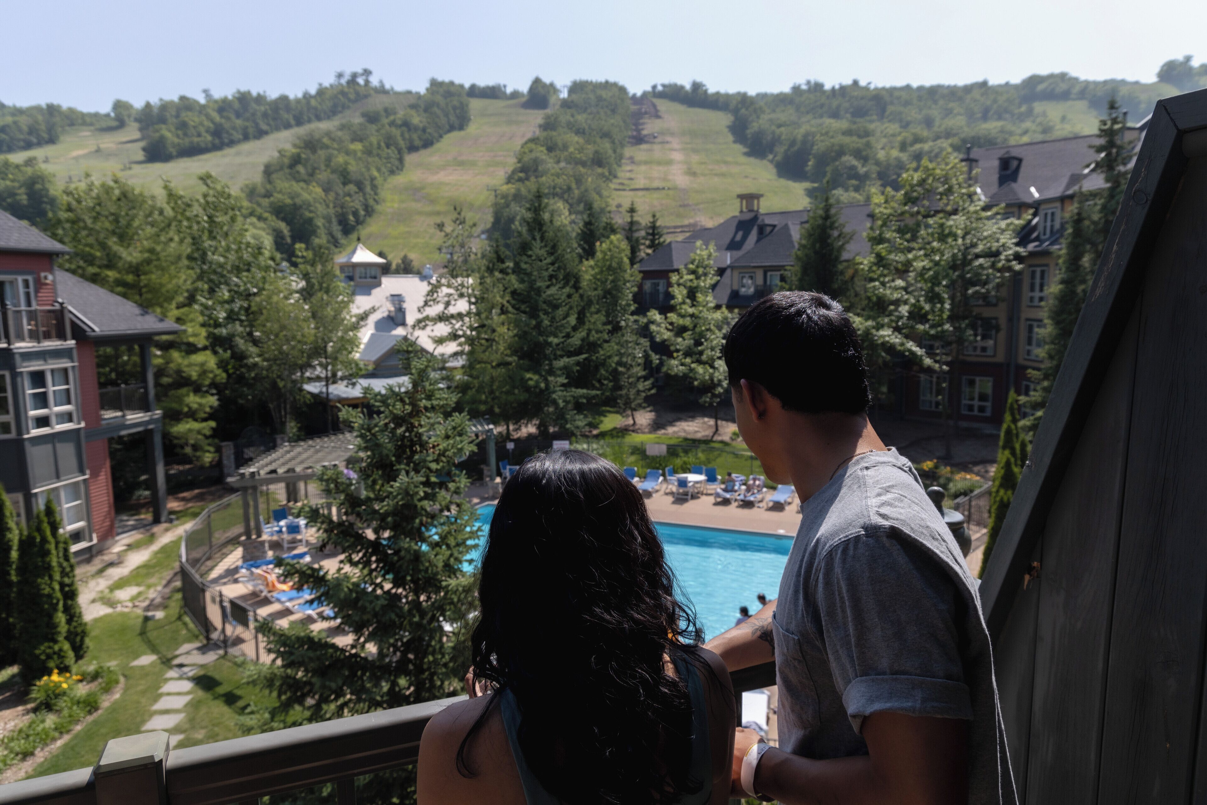 Un balcón con vista a una piscina y un paisaje montañoso con edificios al fondo.