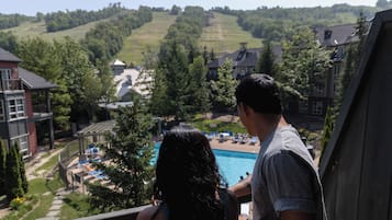 Un balcón con vista a una piscina y un paisaje montañoso con edificios al fondo.