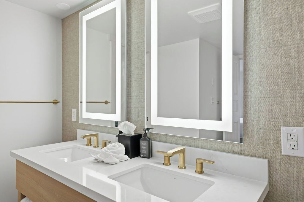 A modern bathroom with two sinks, gold faucets, and a large mirror.