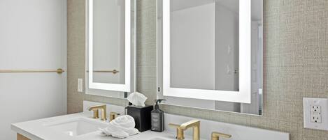 A modern bathroom with two sinks, gold faucets, and a large mirror.