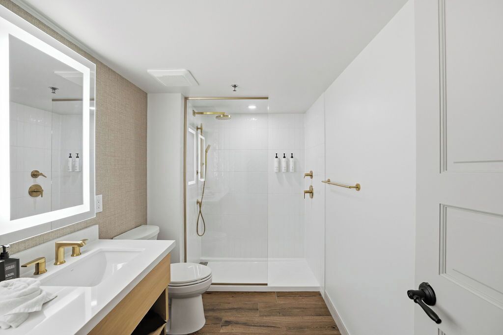 Un baño moderno con ducha de mampara de vidrio, un lavabo blanco y un inodoro.