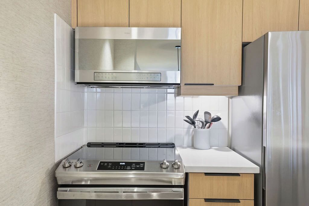 A modern kitchen with stainless steel appliances, wooden cabinets, and a tiled backsplash.