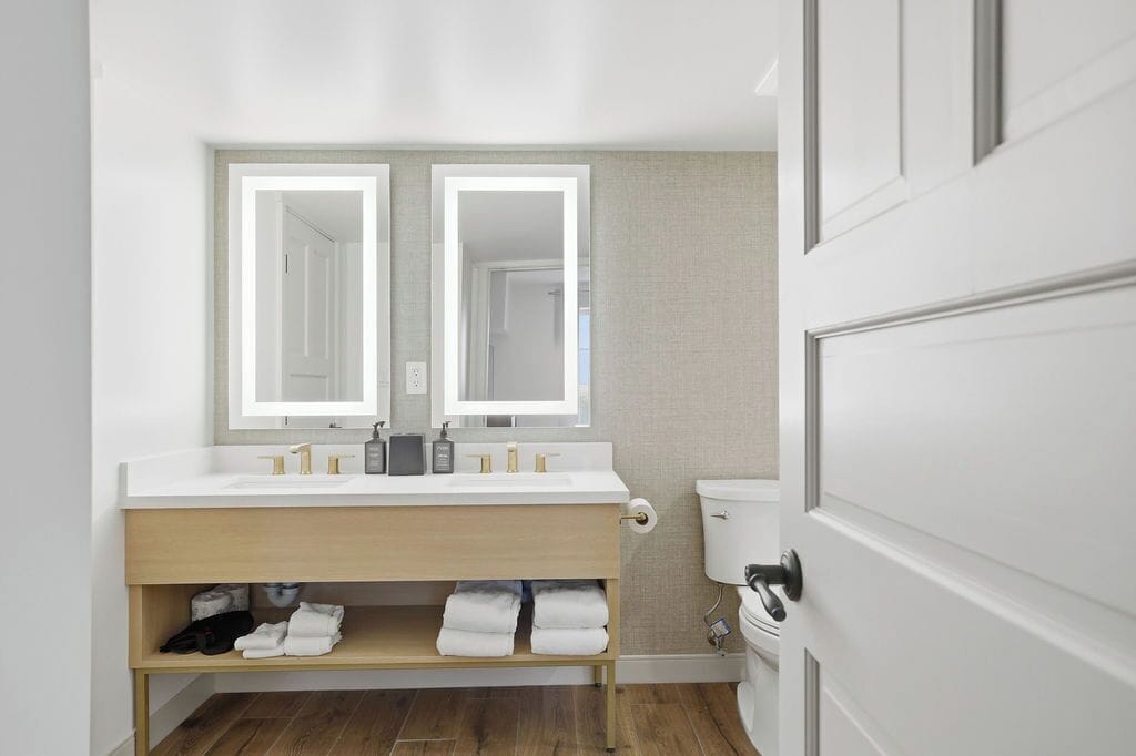 A modern bathroom with a double sink, a toilet, and a towel rack.