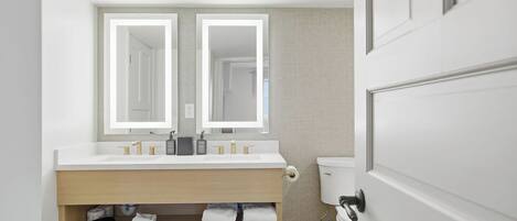 A modern bathroom with a double sink, a toilet, and a towel rack.