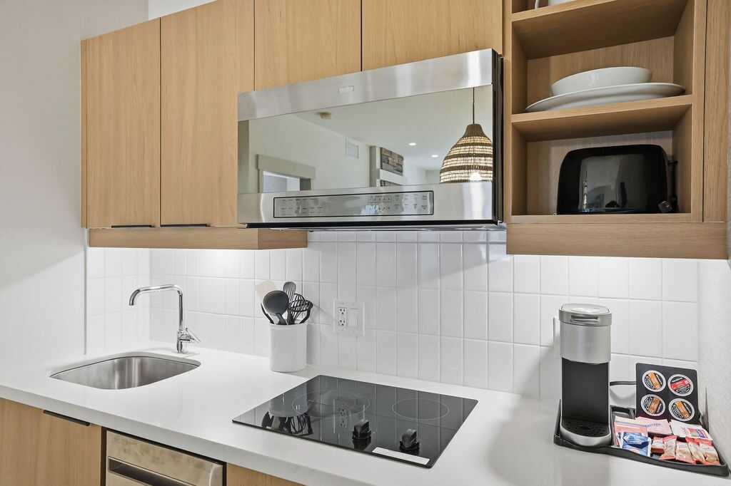 A modern kitchen with a stainless steel range hood, a built-in microwave, a double sink, and a coffee maker.