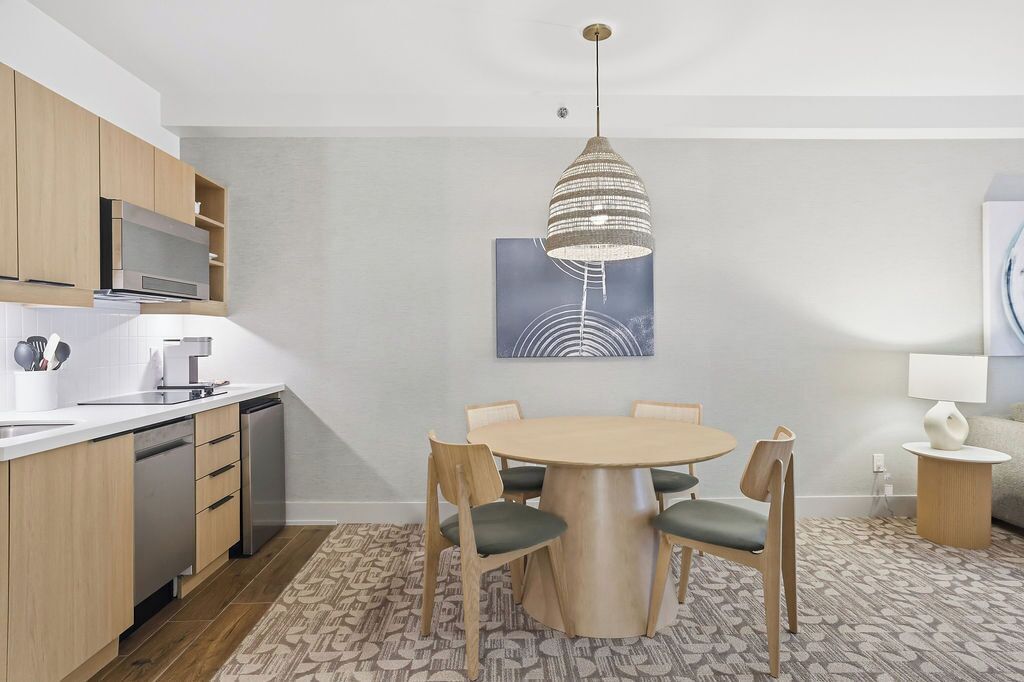 A modern kitchen with wooden cabinets, a built-in microwave, and a dining area with a round table and chairs.