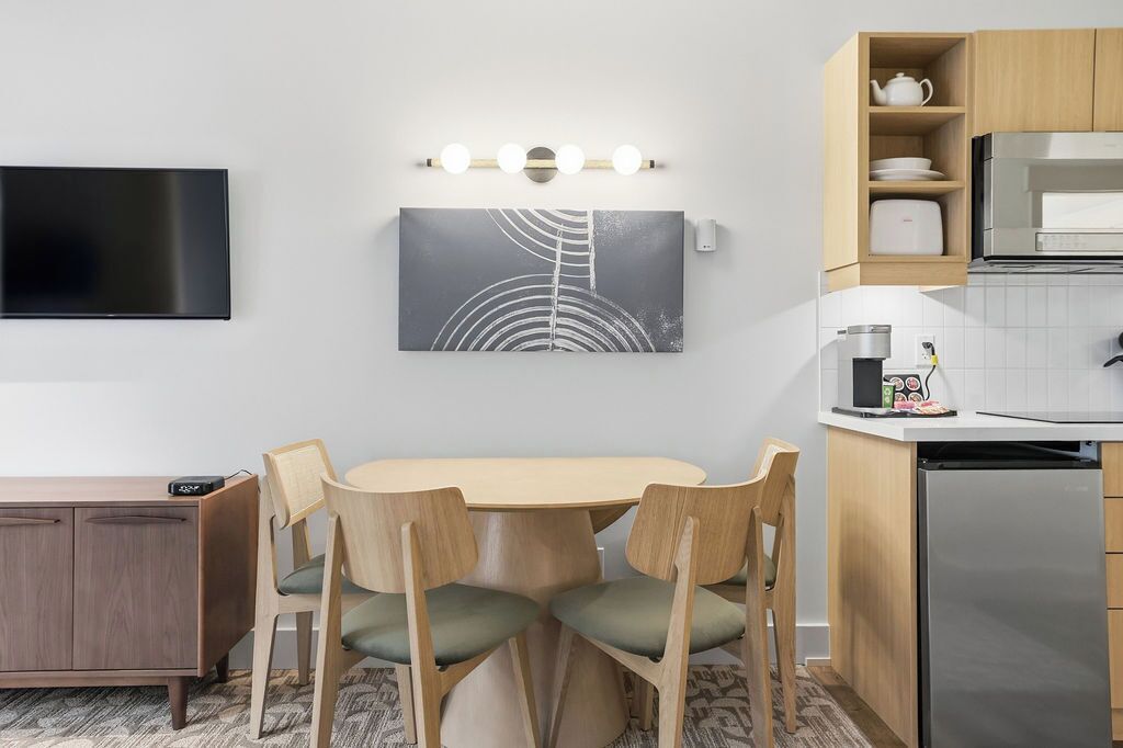 A modern kitchen with a flat-screen TV, a dining table with chairs, a coffee machine, and a microwave.