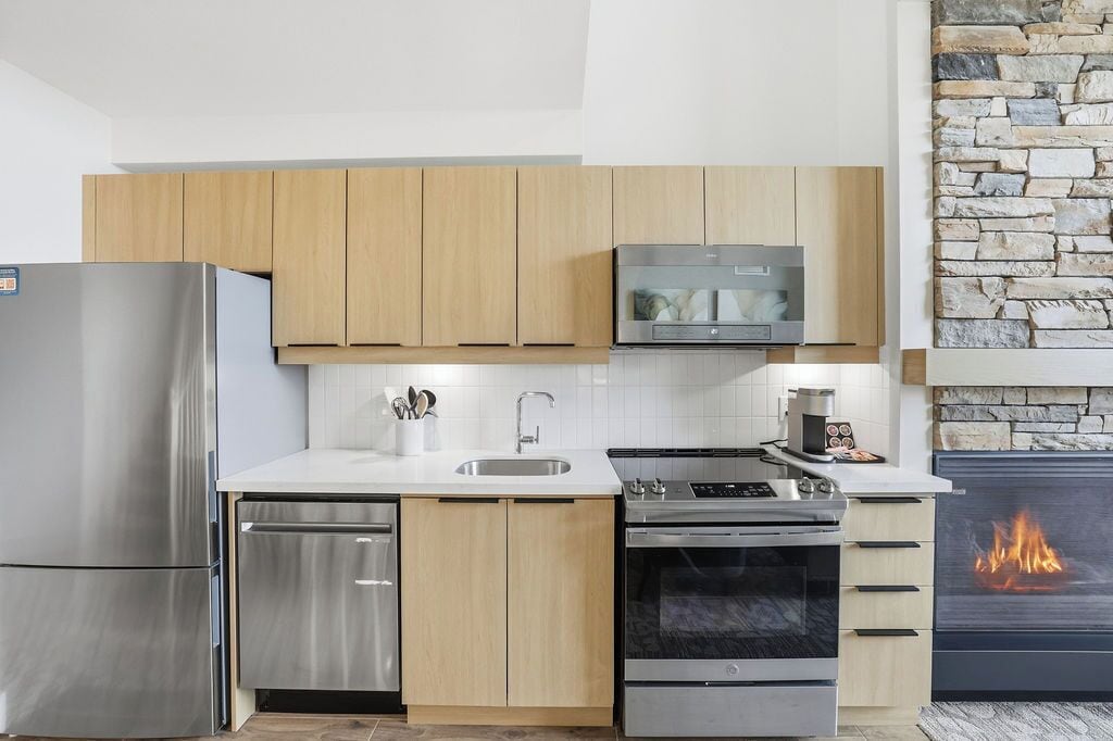 A modern kitchen with stainless steel appliances, wooden cabinets, a stone wall, and a built-in fireplace.