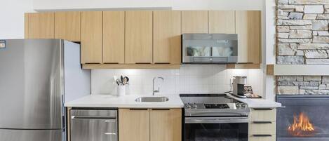 A modern kitchen with stainless steel appliances, wooden cabinets, a stone wall, and a built-in fireplace.