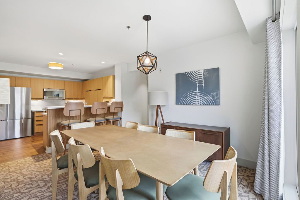 A modern kitchen with wooden cabinets, a dining area with a wooden table and chairs, and a pendant light.