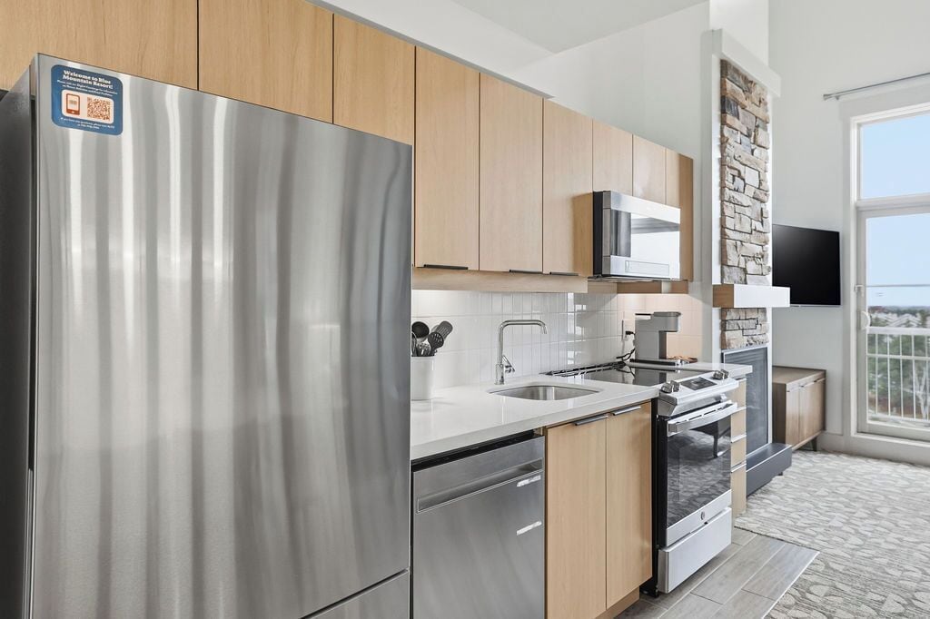 A modern kitchen with stainless steel appliances, wooden cabinets, a built-in microwave, and a stone accent wall.