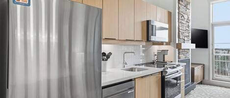 A modern kitchen with stainless steel appliances, wooden cabinets, a built-in microwave, and a stone accent wall.