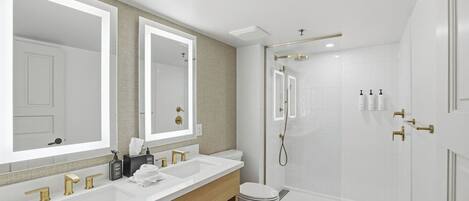 A modern bathroom with a large mirror, two sinks, a toilet, and a walk-in shower.