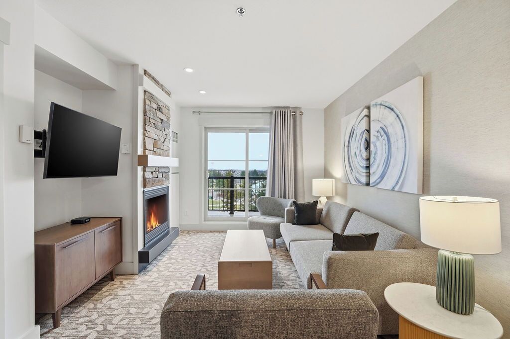 A modern hotel room with a fireplace, a flat-screen TV, a sofa, a coffee table, and a lamp.