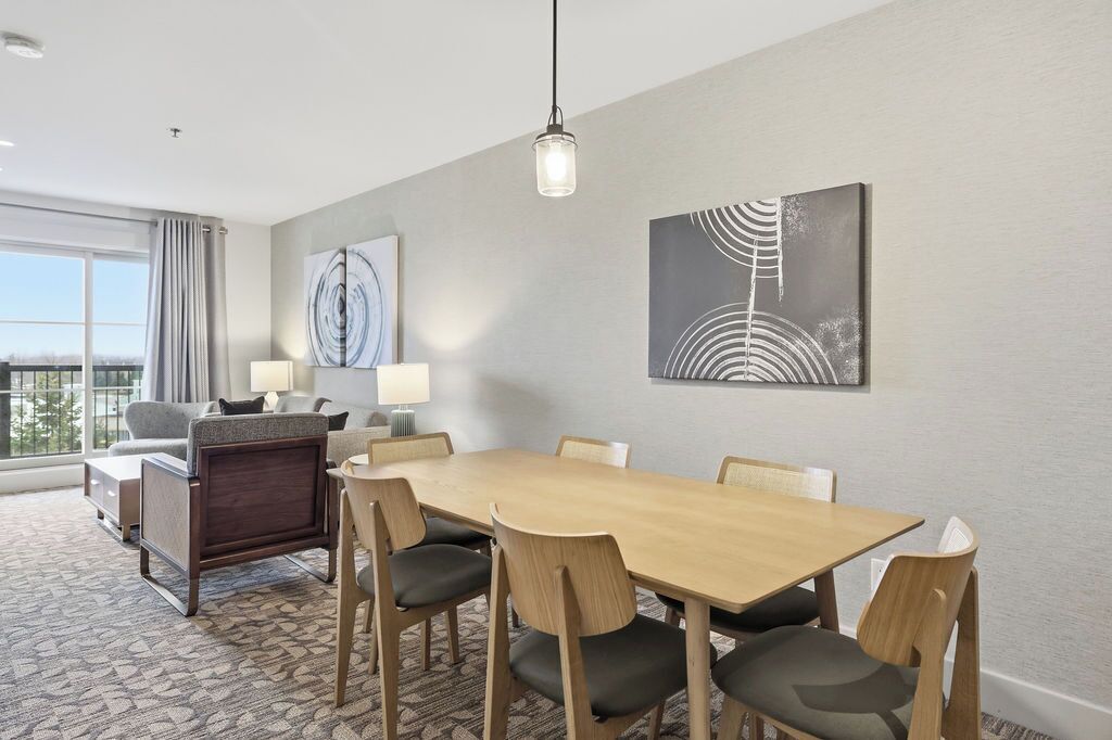 A hotel room with a dining area, a sofa, a lamp, and artwork on the wall.
