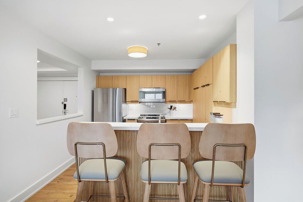 Una cocina moderna con armarios de madera, un refrigerador de acero inoxidable y una isla central con taburetes de bar.