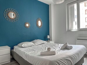 A bedroom with a bed, white nightstands, a window with blinds, and wall decor.