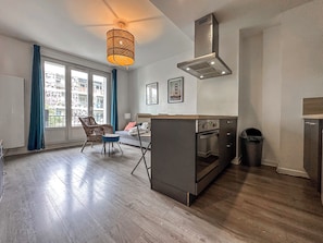 A modern kitchen with a built-in oven, a stainless steel range hood, and a dining area with a chair and table.