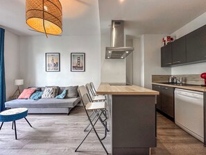 A modern living room with a sofa, chairs, a dining area, and a kitchen with cabinets and a dishwasher.