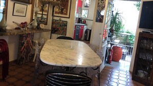 Un coin repas avec une table en marbre, des chaises et un lustre. Des œuvres d’art encadrées ornent les murs, et on peut apercevoir une cuisine à travers une porte ouverte.
