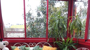 Un coin salon confortable avec une fenêtre à cadre rouge, une table basse en verre et divers coussins.
