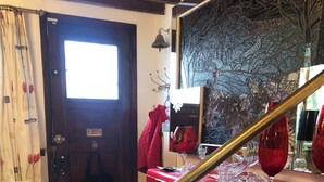 Un escalier avec une rampe en laiton menant à un meuble rouge, une chaise blanche avec un coussin à motifs léopard et une porte avec une fenêtre.