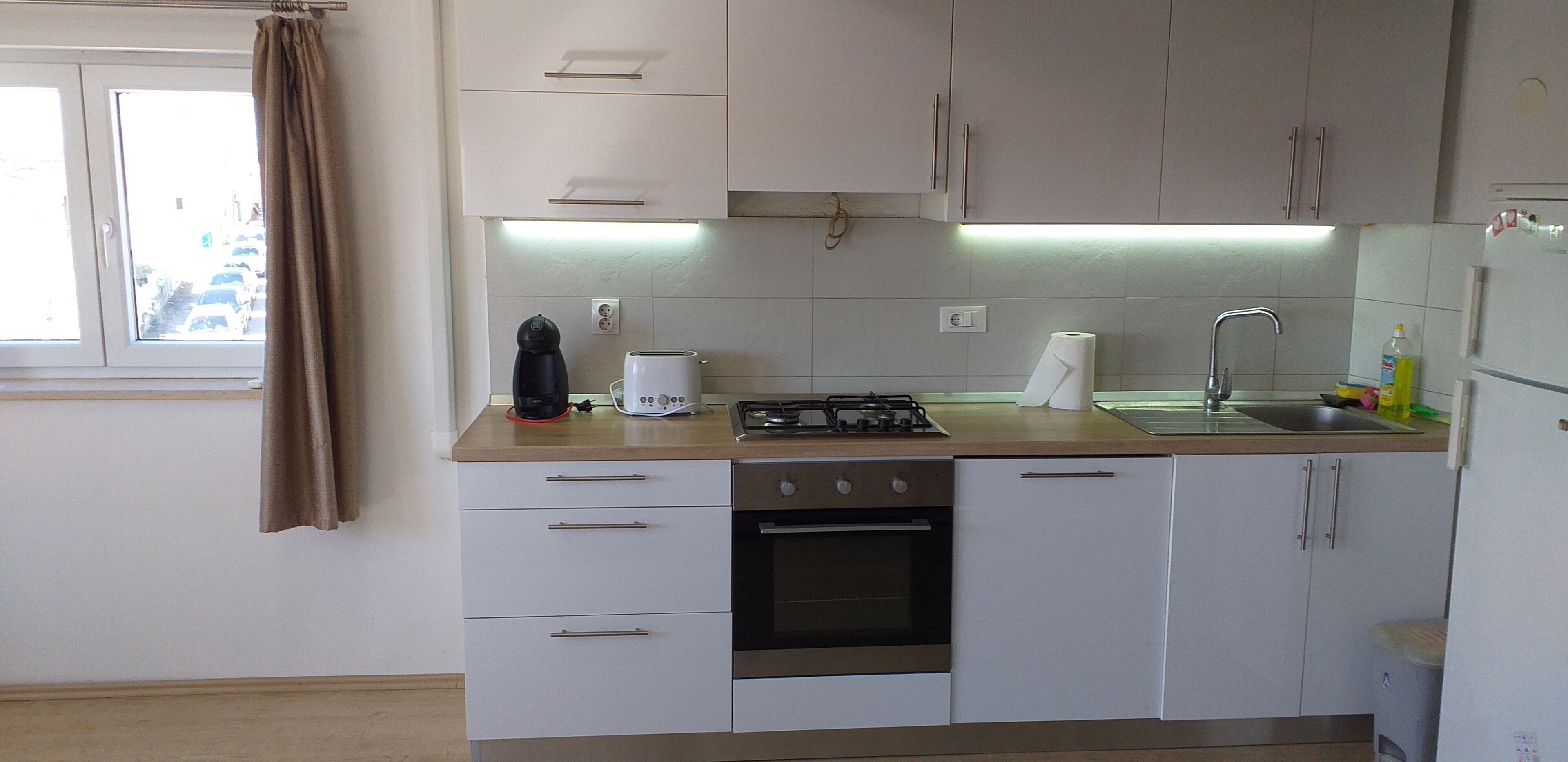 Una cucina moderna con mobili bianchi, piano cottura a gas, macchina da caffè e lavello.