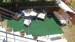 Een terras op het dak met een ronde tafel, twee stoelen, een bank en potplanten.
