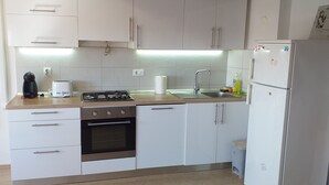 Een kleine keuken met witte kasten, een gasfornuis, een spoelbak en een koelkast.