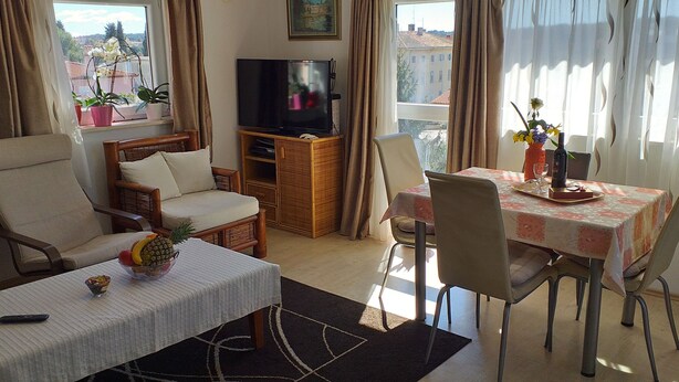 Een woonkamer met een televisie, een eettafel met stoelen, een bank en een salontafel met een ananas.