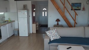 Een compacte keuken met een koelkast, fornuis en wastafel. Een houten trap leidt naar een woonruimte met een bank en een lamp.
