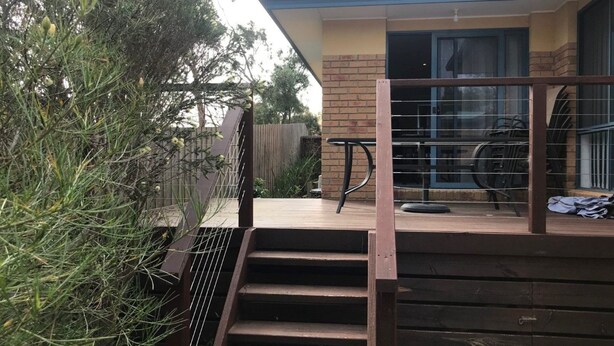 Una escalera de madera que lleva a una terraza con barandilla de metal, un muro de ladrillo y una ventana.