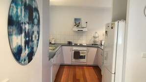 Cocina compacta con armarios blancos, horno empotrado, refrigerador blanco y piso de madera.