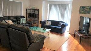 Una sala de estar con un sofá modular, un sofá más pequeño, una mesa de centro y un televisor sobre un mueble.