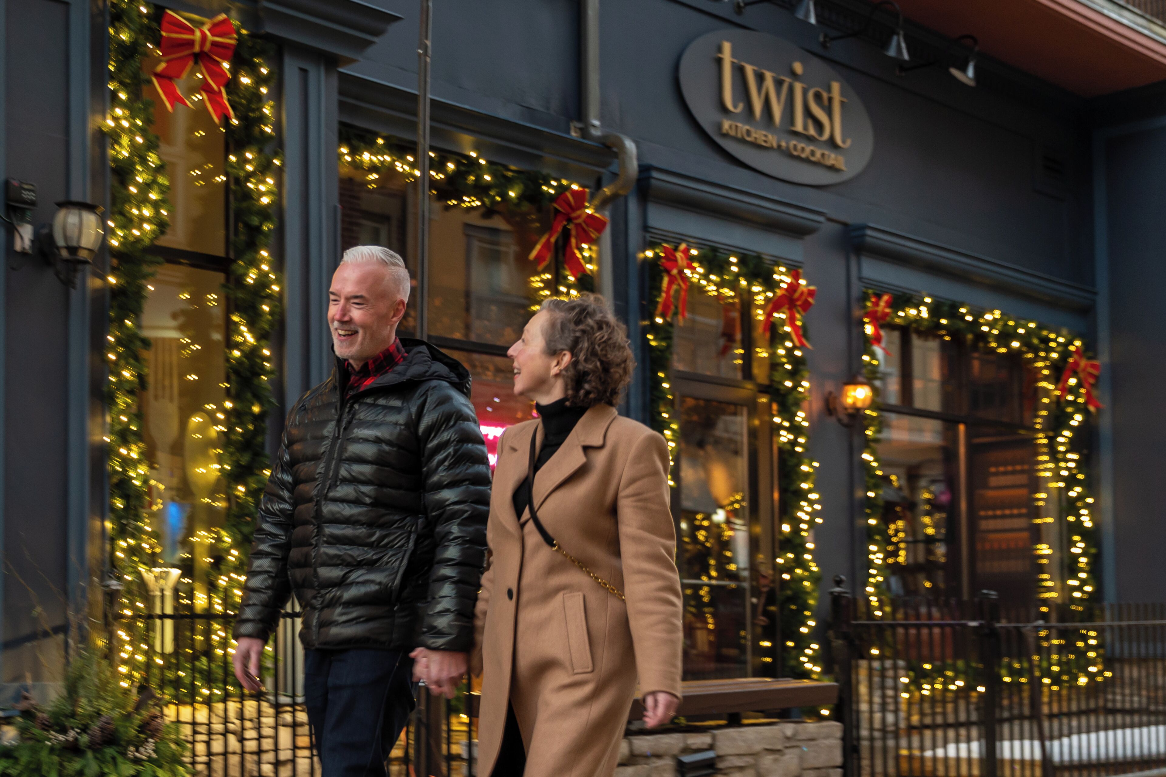 A couple standing in front of a building with a sign that reads "twist kitchen & cocktail."