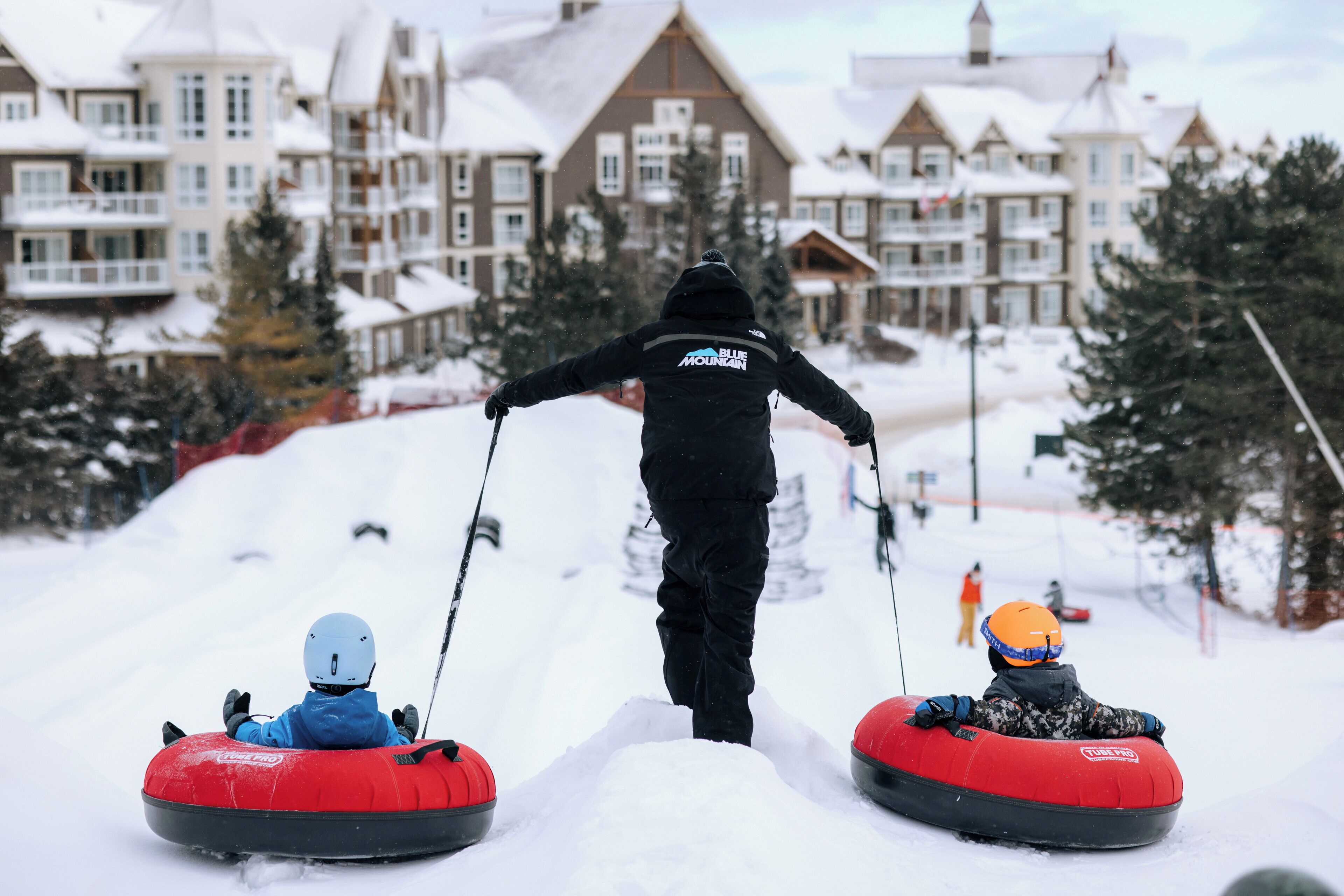 A person leading two children on snow tubes down a snowy slope.