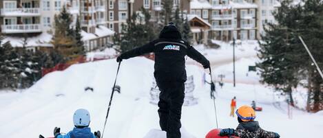 A person leading two children on snow tubes down a snowy slope.