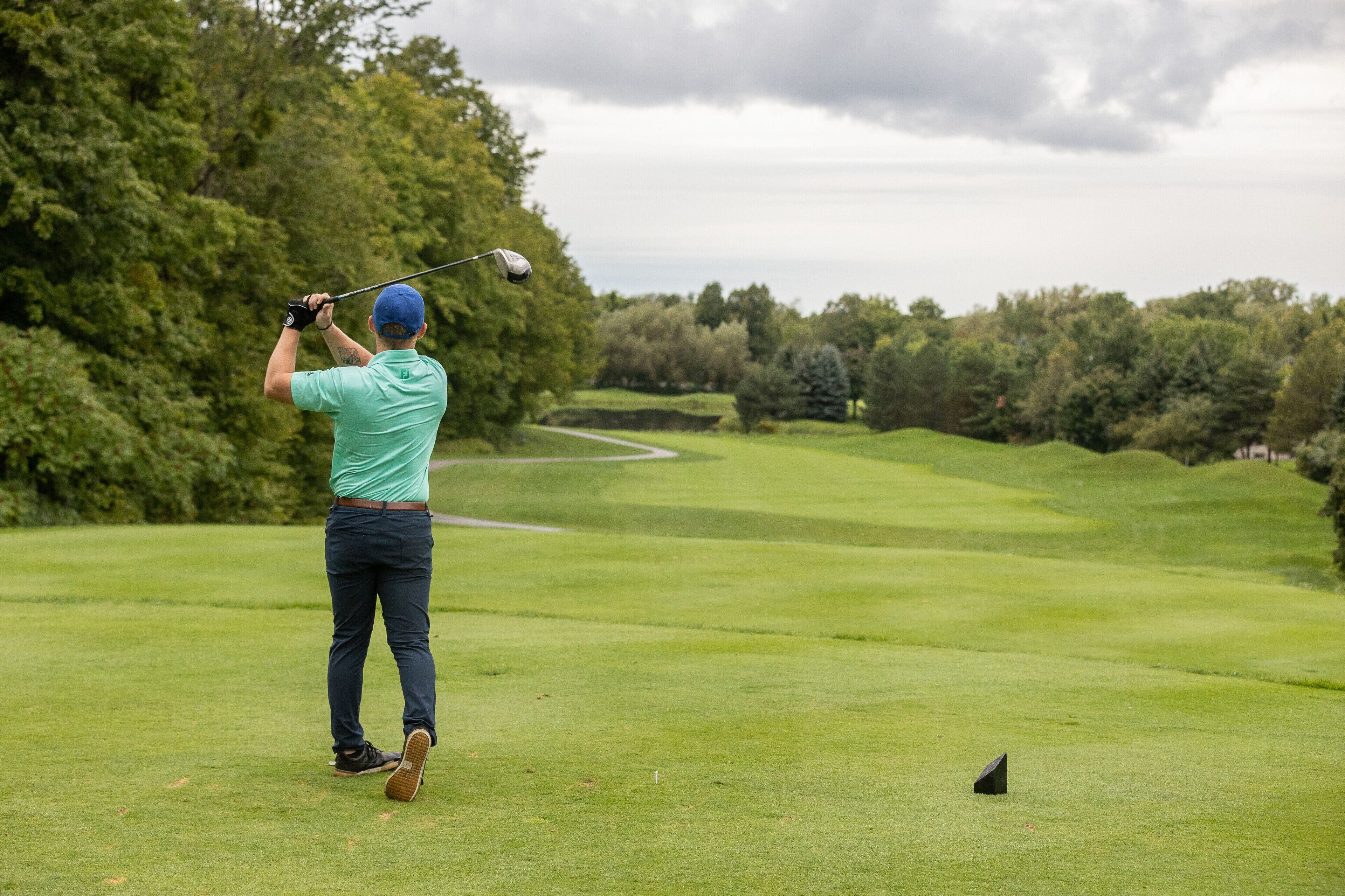 Una persona juga a golf en un camp ben cuidat, ple d'arbres i amb un cel clar.