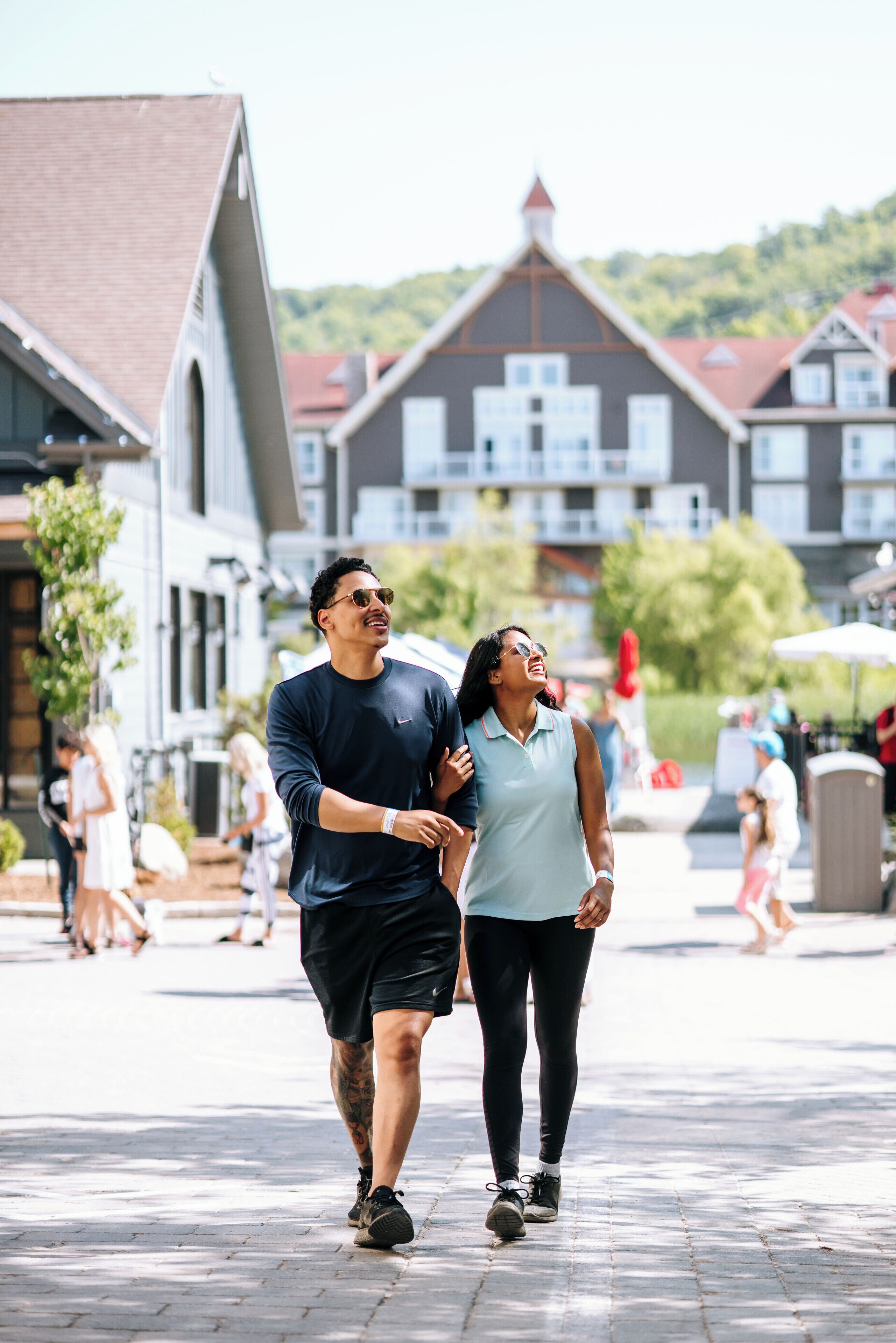 Two people walking on a paved path in a town square with buildings in the background.