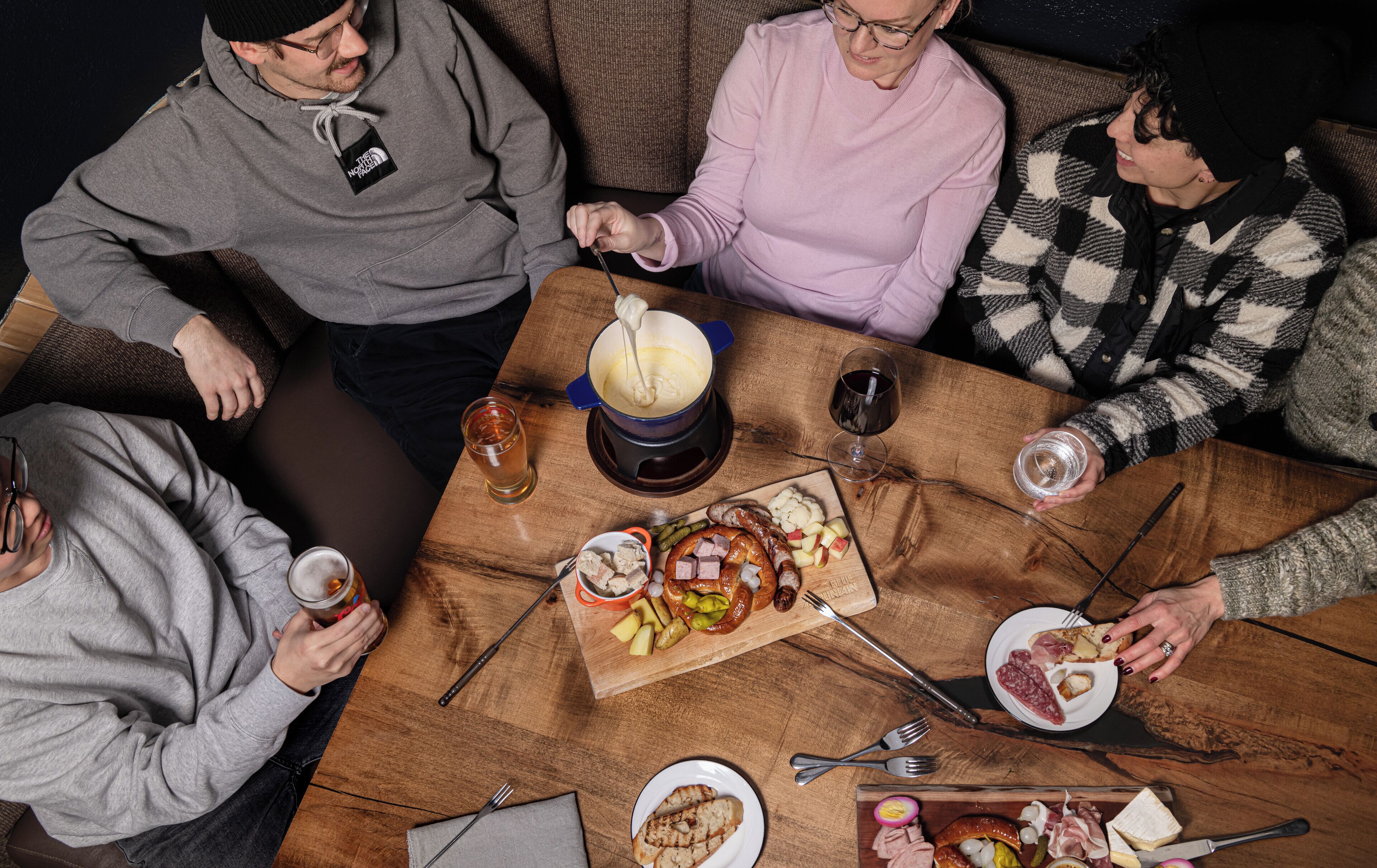 A group of people seated around a wooden table with a variety of food items and drinks.