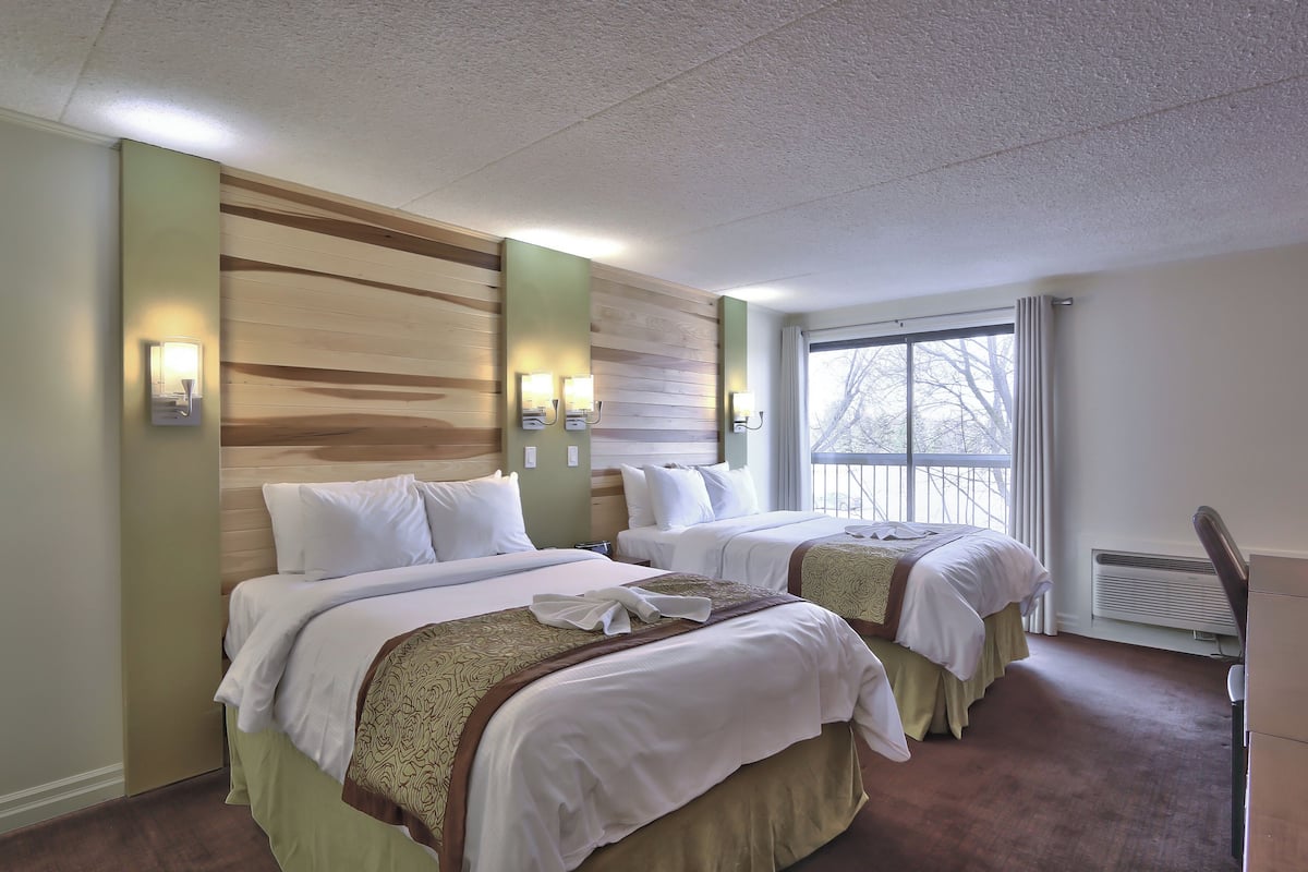 A hotel room with two beds, a large window, and a built-in heater.