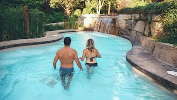 A man and a woman walking in a pool with a waterfall feature.