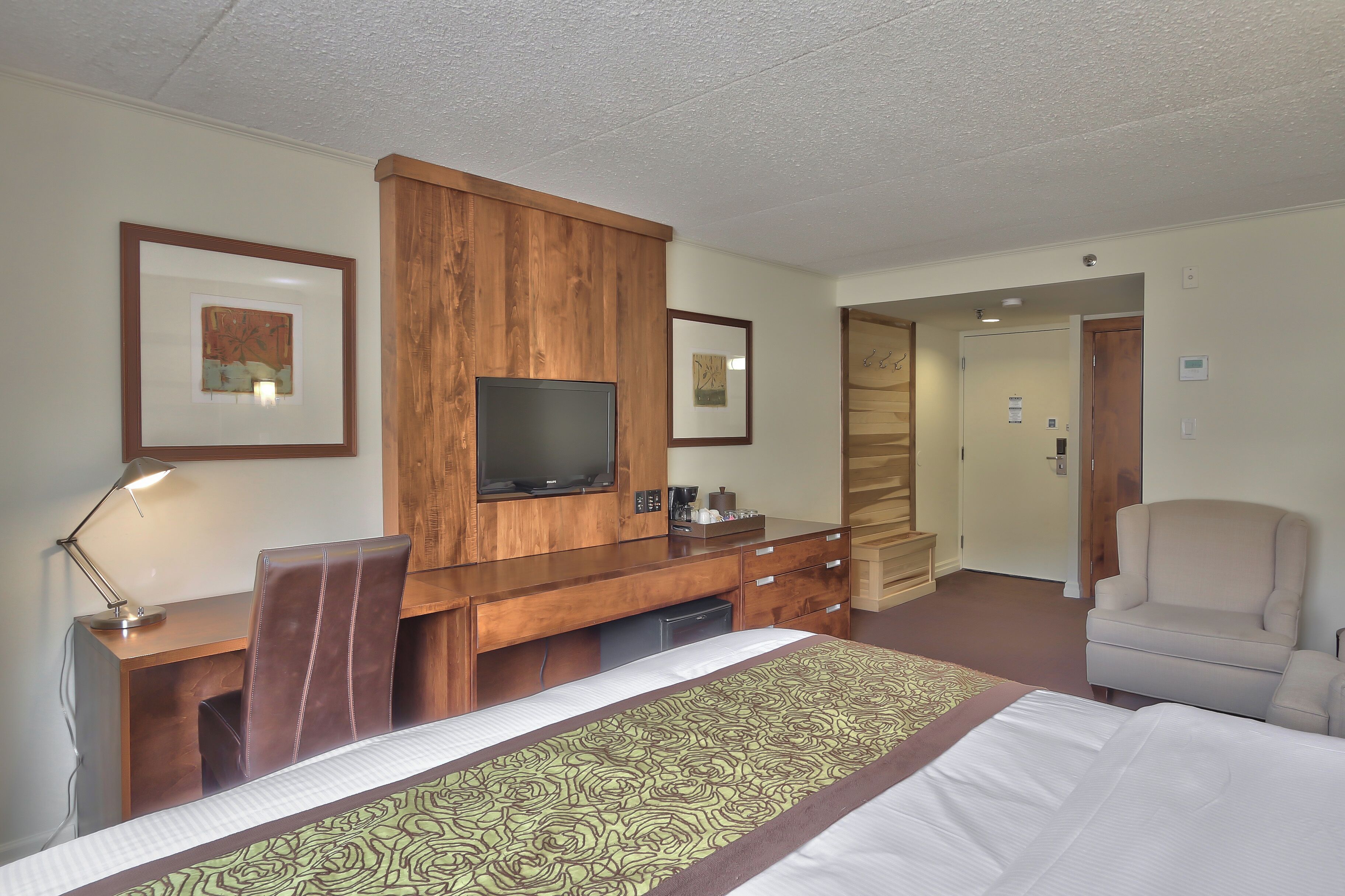 A hotel room with a bed, a desk with a television, a chair, and a wardrobe.