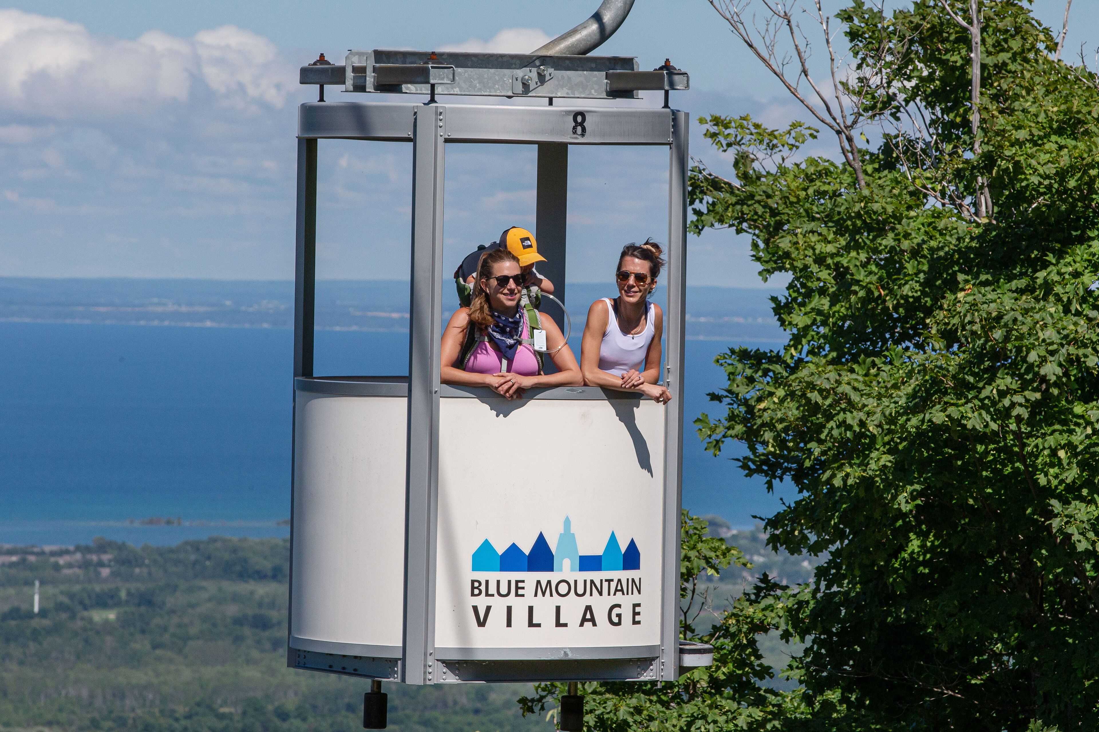 A cable car with two passengers, labeled "Blue Mountain Village," offering a scenic view of the landscape.