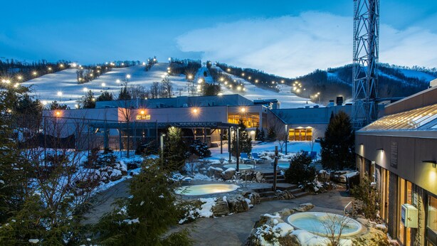 A winter resort with a snow-covered landscape, a pool area, and a building with illuminated windows. - Blue Mountain Resort Inn (The Blue Mountains)