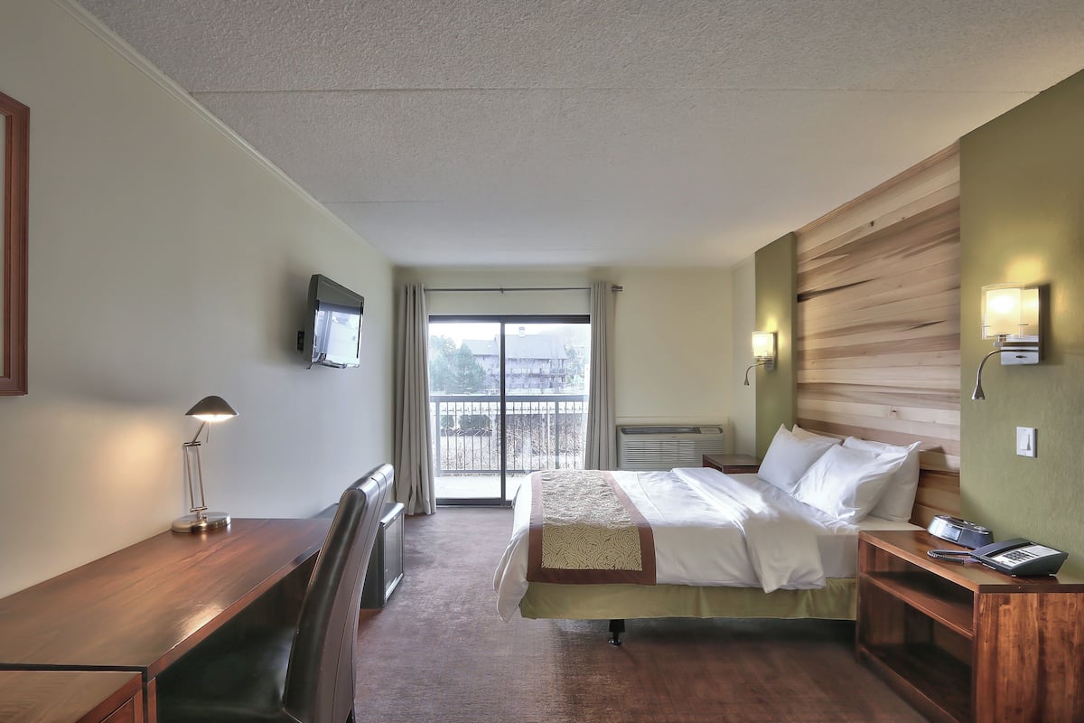 A hotel room with a bed, bedside table, lamp, and a TV on the wall.