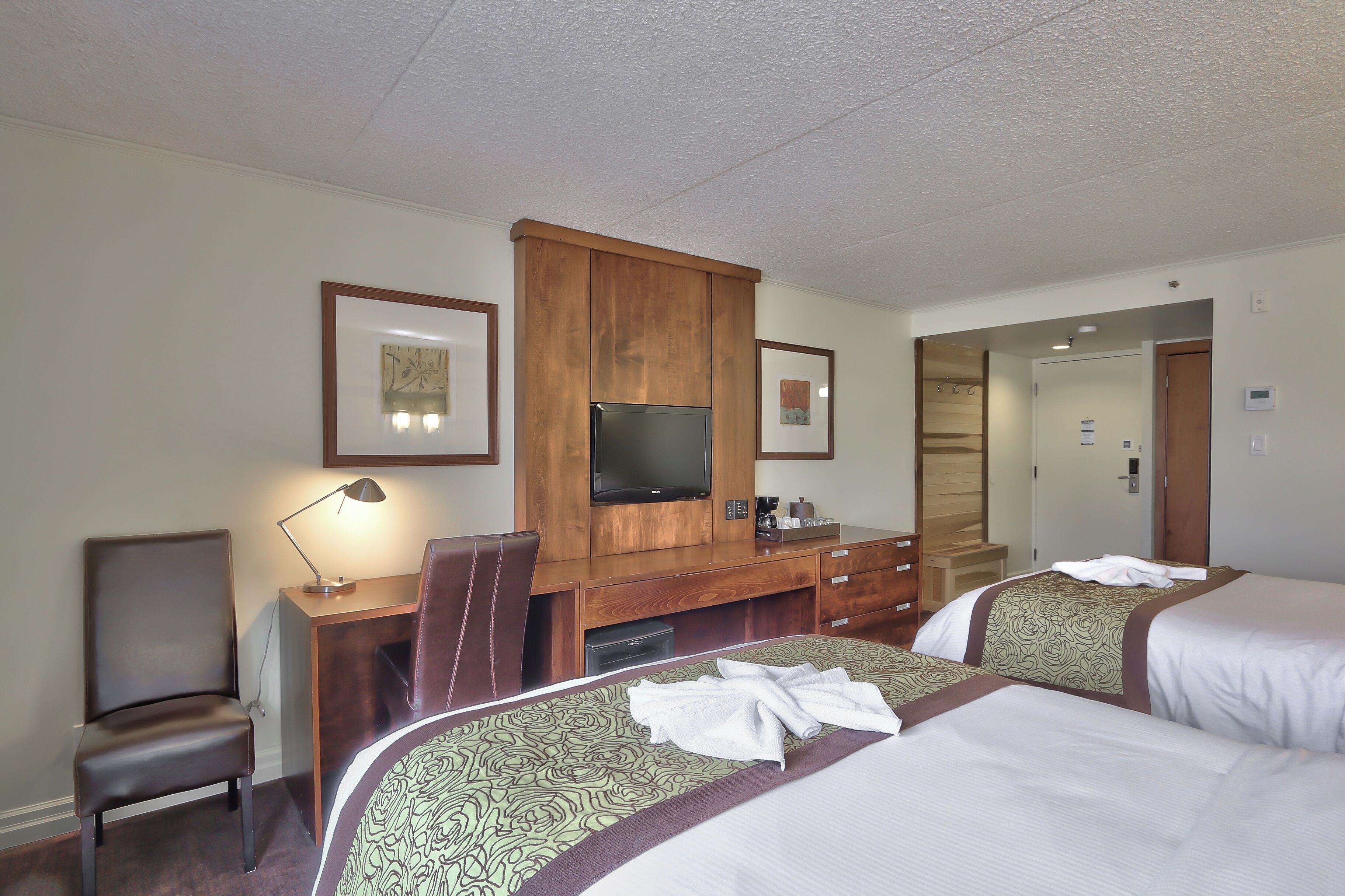 A hotel room with a bed, a desk, a chair, a television, and a mirror.